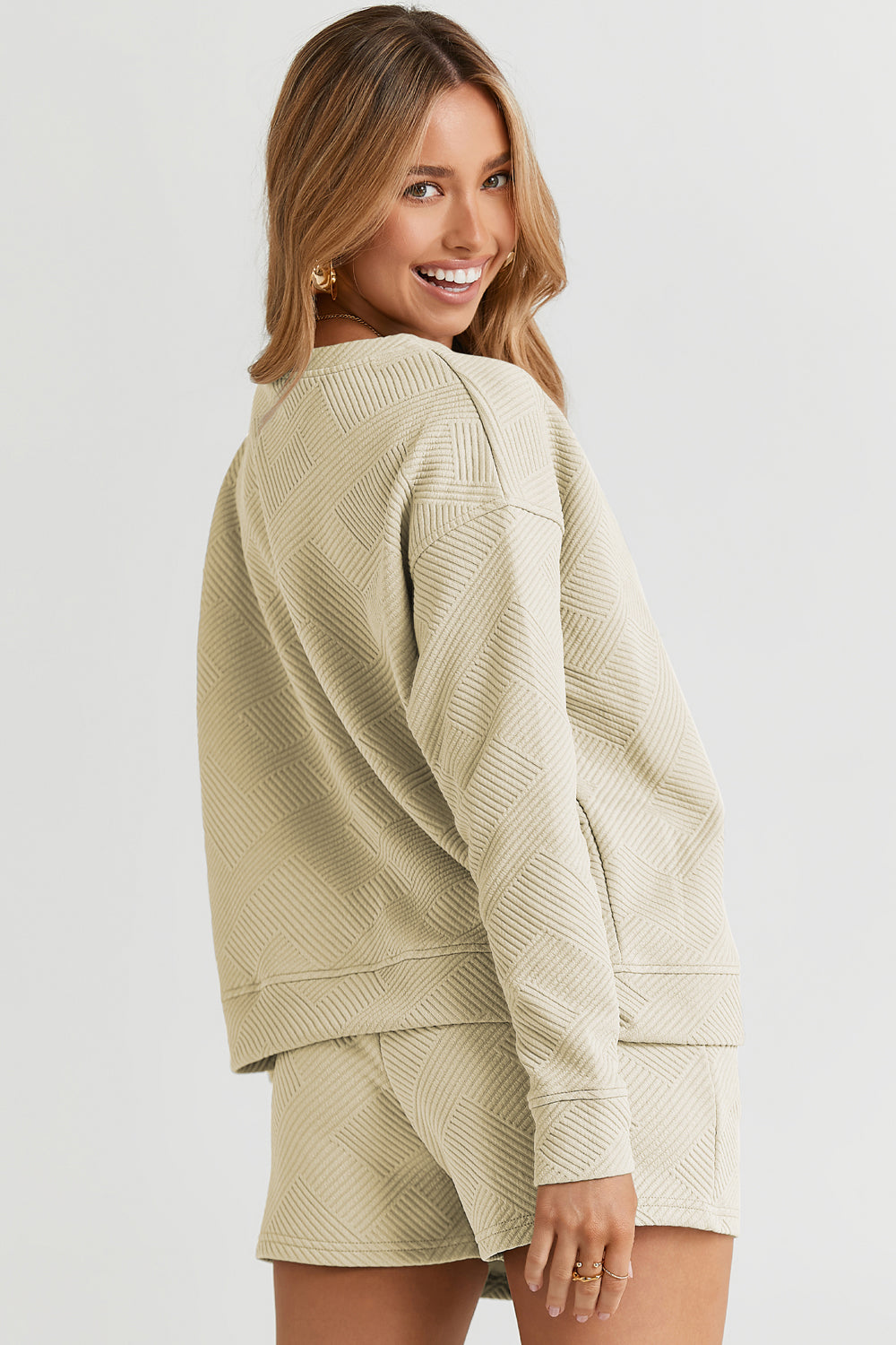 Woman wearing a beige textured long sleeve top and drawstring shorts set with pockets, slightly stretchy polyester-spandex blend.