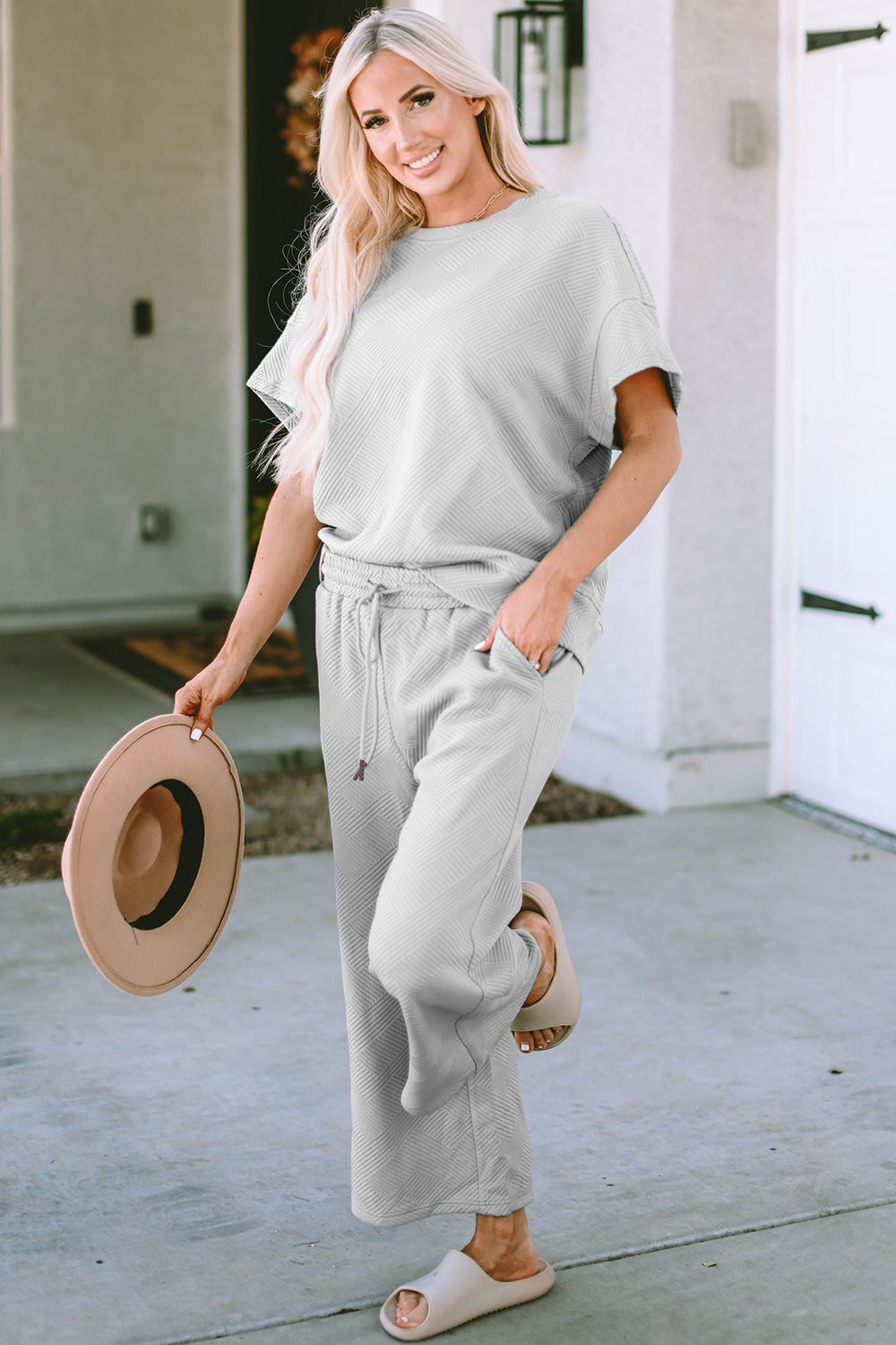 Woman wearing a drawstring short sleeve top and pants set made of slightly stretchy fabric with hat and casual sandals.