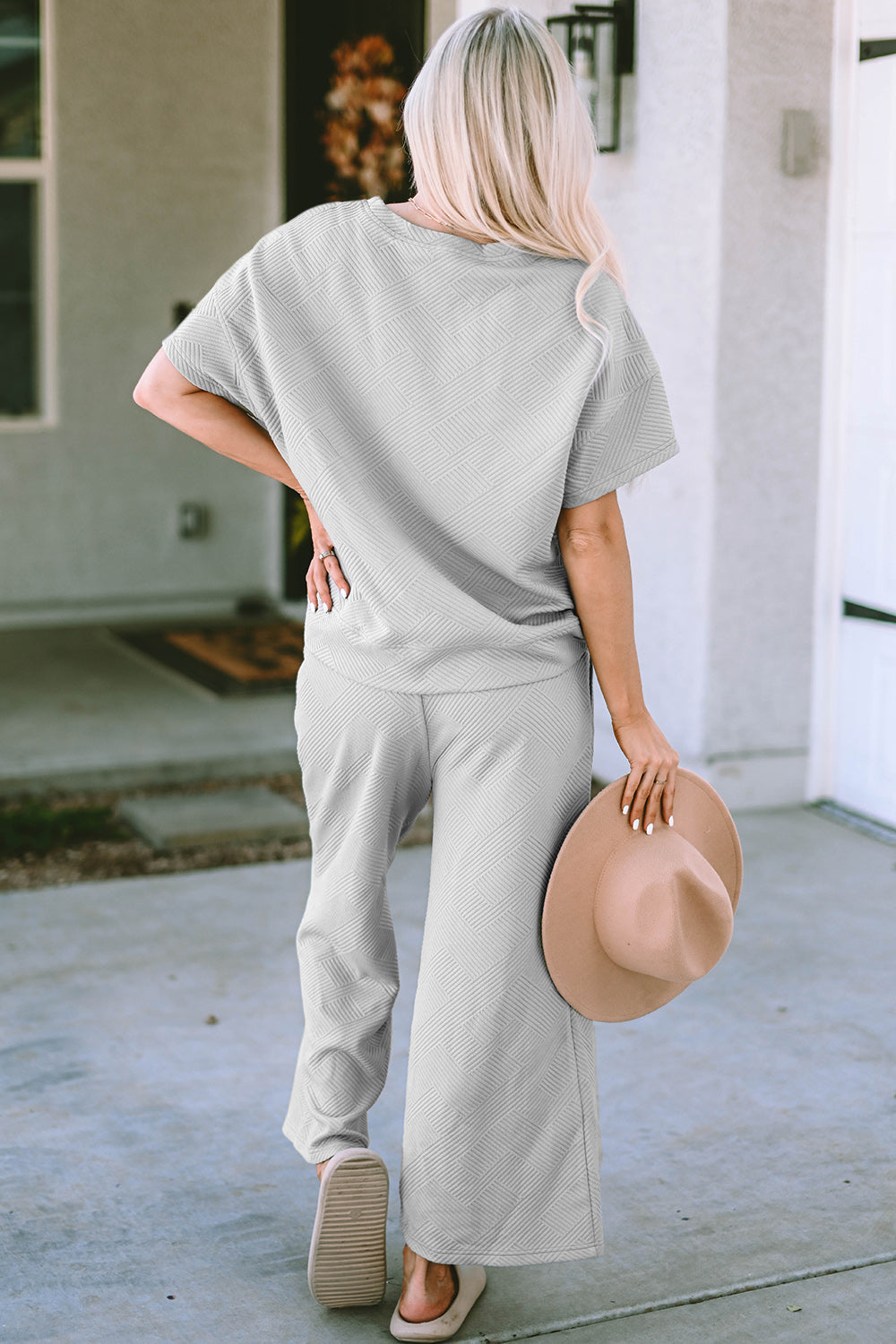 Woman in a texture short sleeve top and pants set, holding a hat, featuring a drawstring design and slightly stretchy fabric.