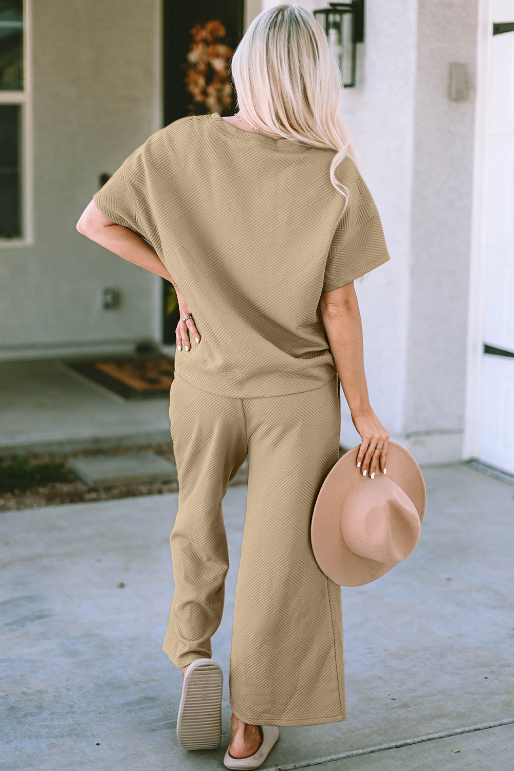 Woman wearing beige texture short sleeve top and pants set holding a hat, showcasing casual two-piece outfit with slight stretch.