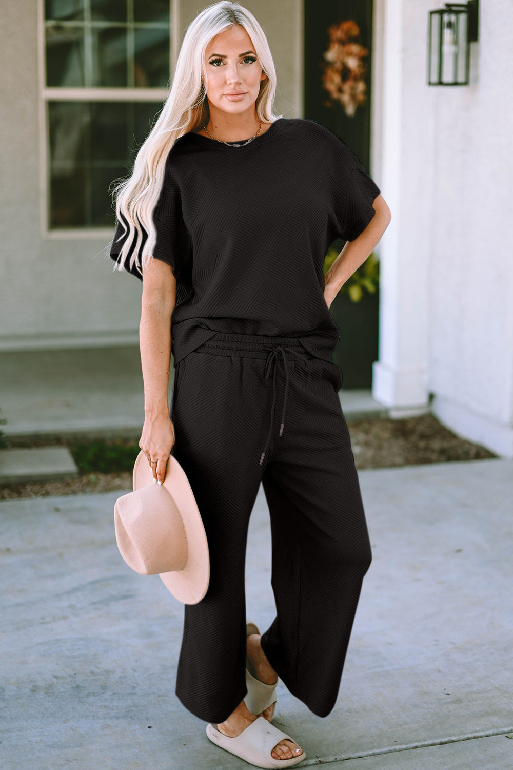 Woman wearing black texture short sleeve top and pants set with drawstring, holding a hat in a casual outdoor setting.