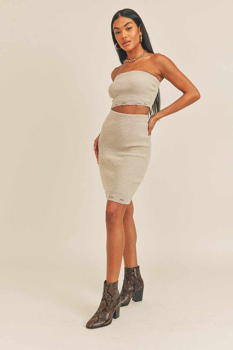 Stylish woman wearing a beige crop trendy two-piece set with tube top and high-rise pencil skirt, paired with ankle boots.