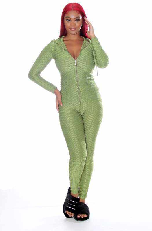 Woman wearing green zip-up jumpsuit with red hair, posing confidently in black sandals.