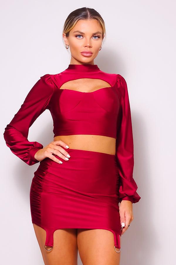 Woman wearing red turtleneck blouse with puff sleeves and side ruched mini skirt set, featuring front cutout and garter strap details.