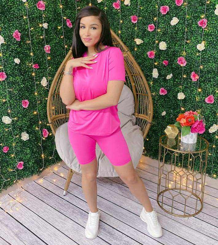 Woman wearing Neon Barbie Two-Piece Set made of 96% polyester and 4% spandex, standing in a garden setting with floral decor.