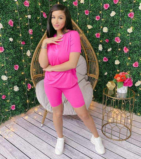 Woman wearing Neon Barbie Two-Piece Set made of 96% polyester and 4% spandex, standing in a garden setting with floral decor.