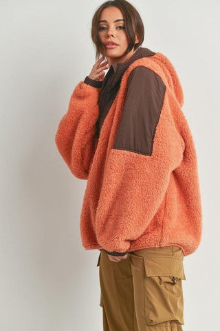 Woman wearing orange and brown two-toned cozy hooded sweater made of 100% polyester, paired with cargo pants.