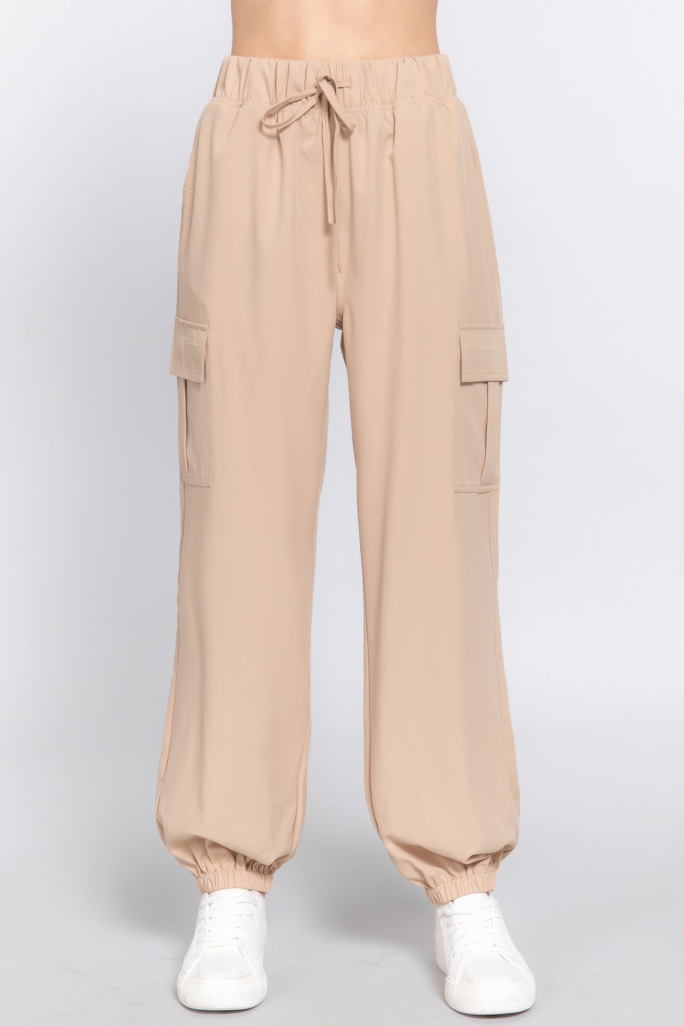 Beige lightweight stretch woven cargo jogger pants with elastic ankle cuffs and utility pockets, paired with white sneakers.