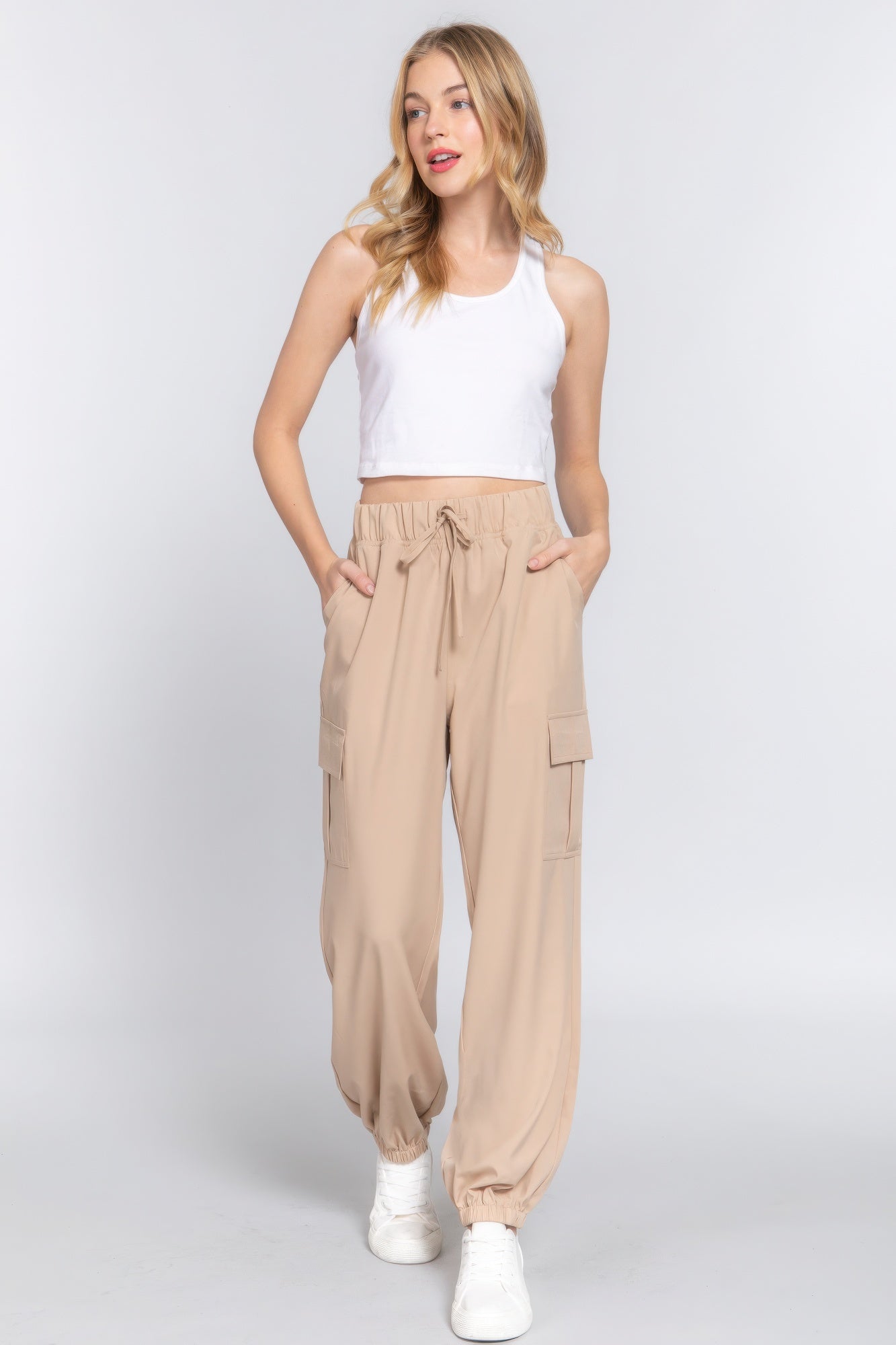 Woman wearing lightweight stretch woven cargo jogger pants in beige, paired with a white tank top and sneakers for a casual look.