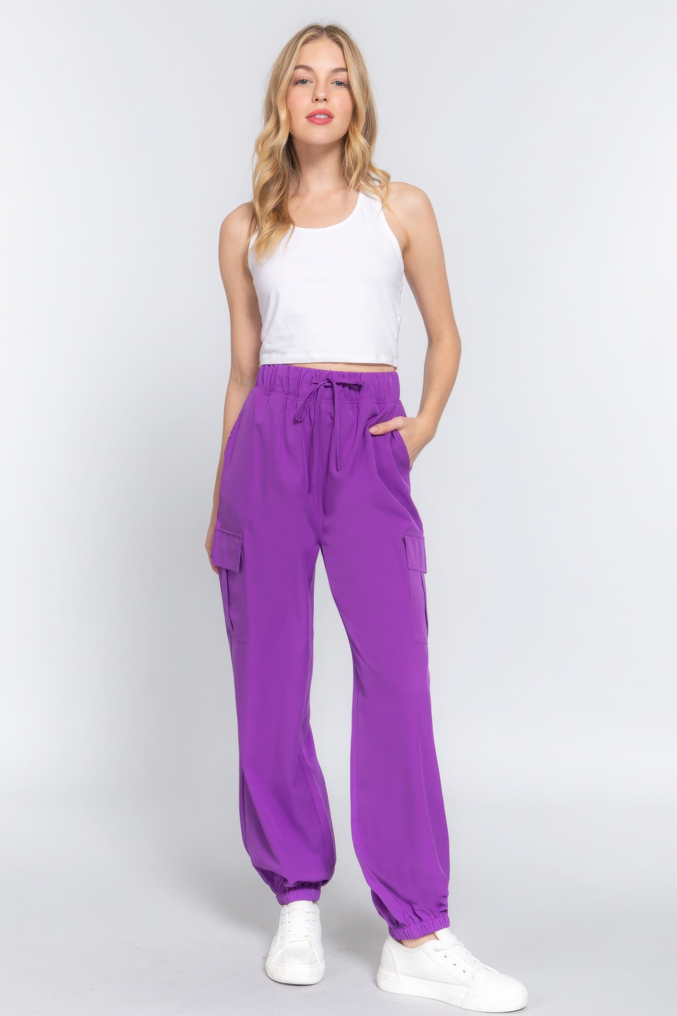 Woman wearing purple lightweight stretch woven cargo jogger pants with trendy pockets, paired with a white tank top and sneakers.