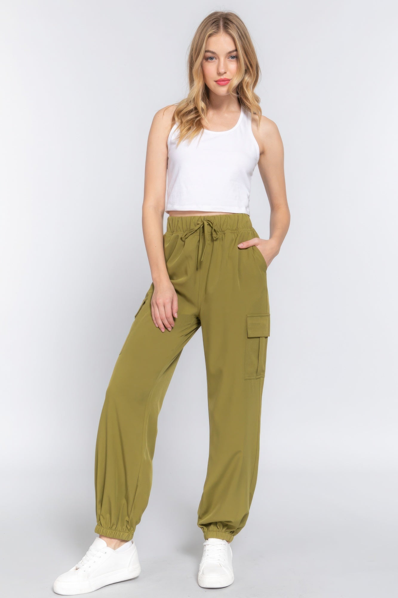 Woman wearing lightweight stretch woven cargo jogger pants in olive green with cargo pockets, styled with a white tank top.