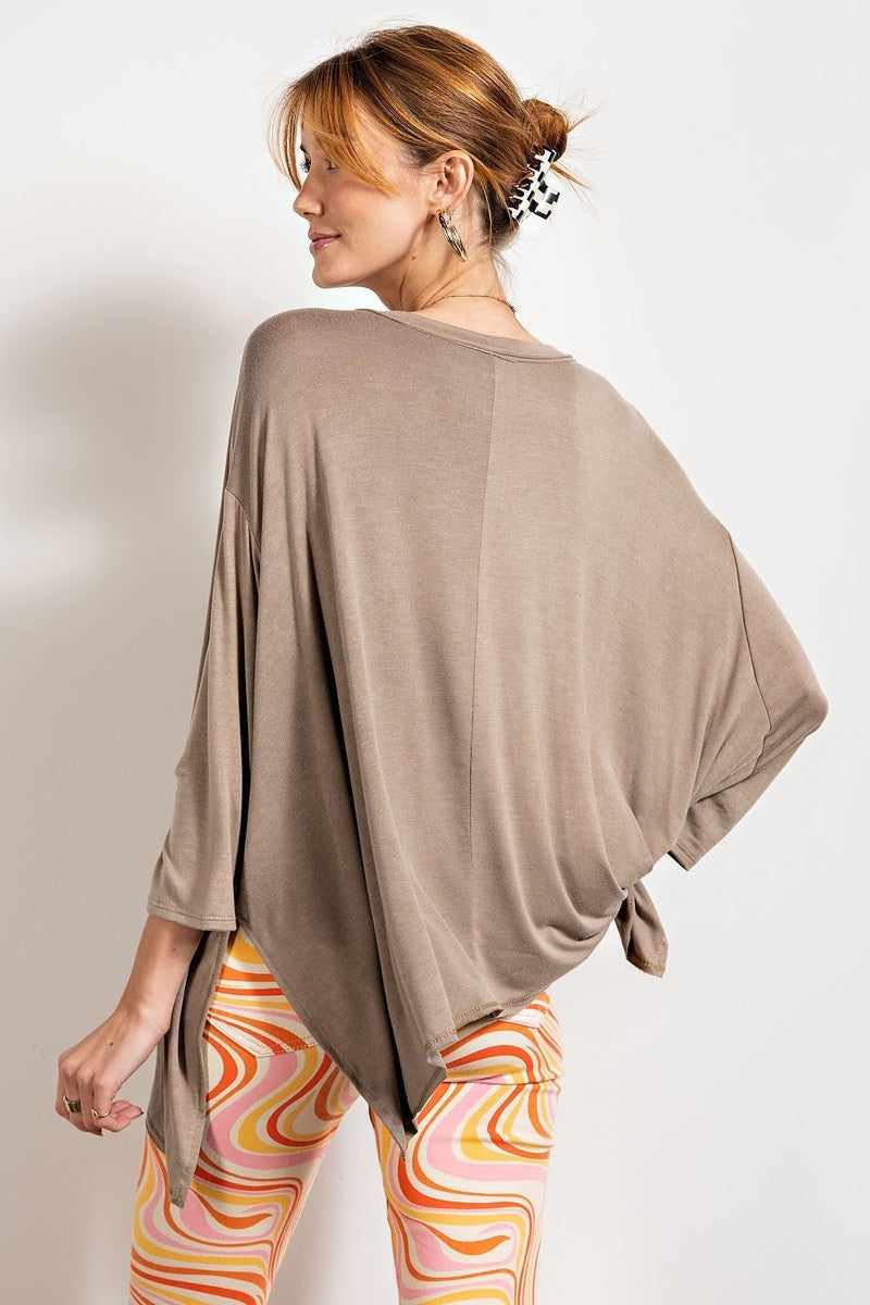 Woman wearing oversized mushroom brown washed top with rounded neckline and 3/4 sleeves, styled with vibrant swirl-patterned leggings.