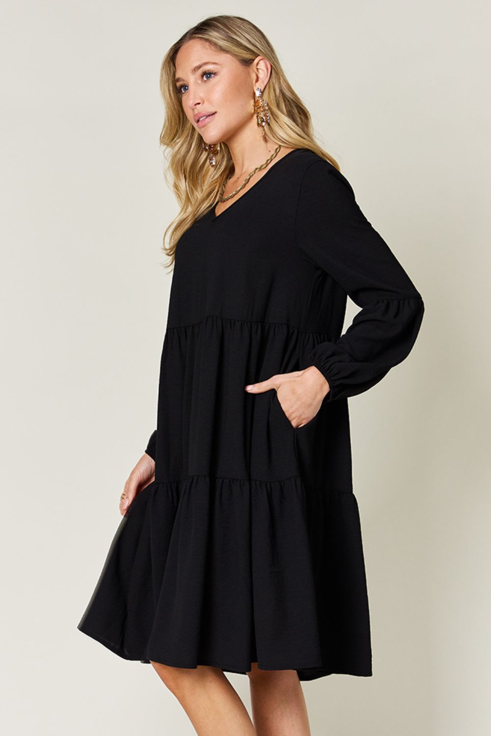 Woman wearing a black V-neck balloon sleeve tiered dress with pockets and ruffled details.