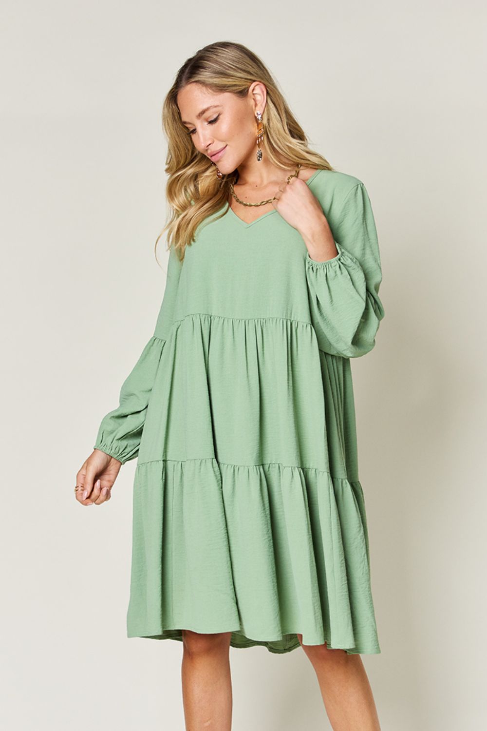 Woman wearing green V-neck balloon sleeve tiered dress with pockets, made of 100% high stretch yarn, featuring ruffled design.