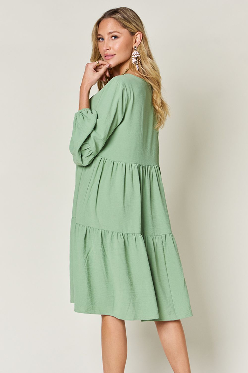 Woman wearing a green V-Neck Balloon Sleeve Tiered Dress with Pockets, showing ruffled and pocketed design on opaque fabric.