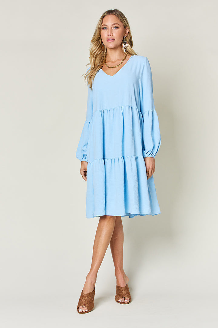 Woman wearing a blue V-neck balloon sleeve tiered dress with pockets, ideal for a stylish and comfortable look.