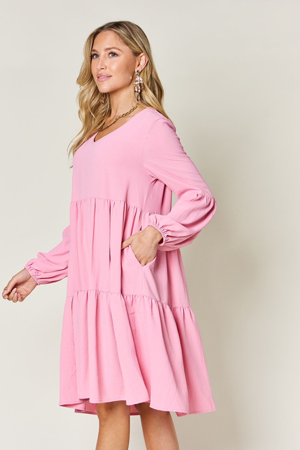 Woman wearing pink V-neck balloon sleeve tiered dress with pockets.