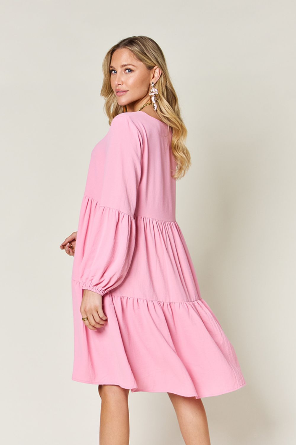 Woman wearing pink V-neck balloon sleeve tiered dress with pockets and ruffled details.