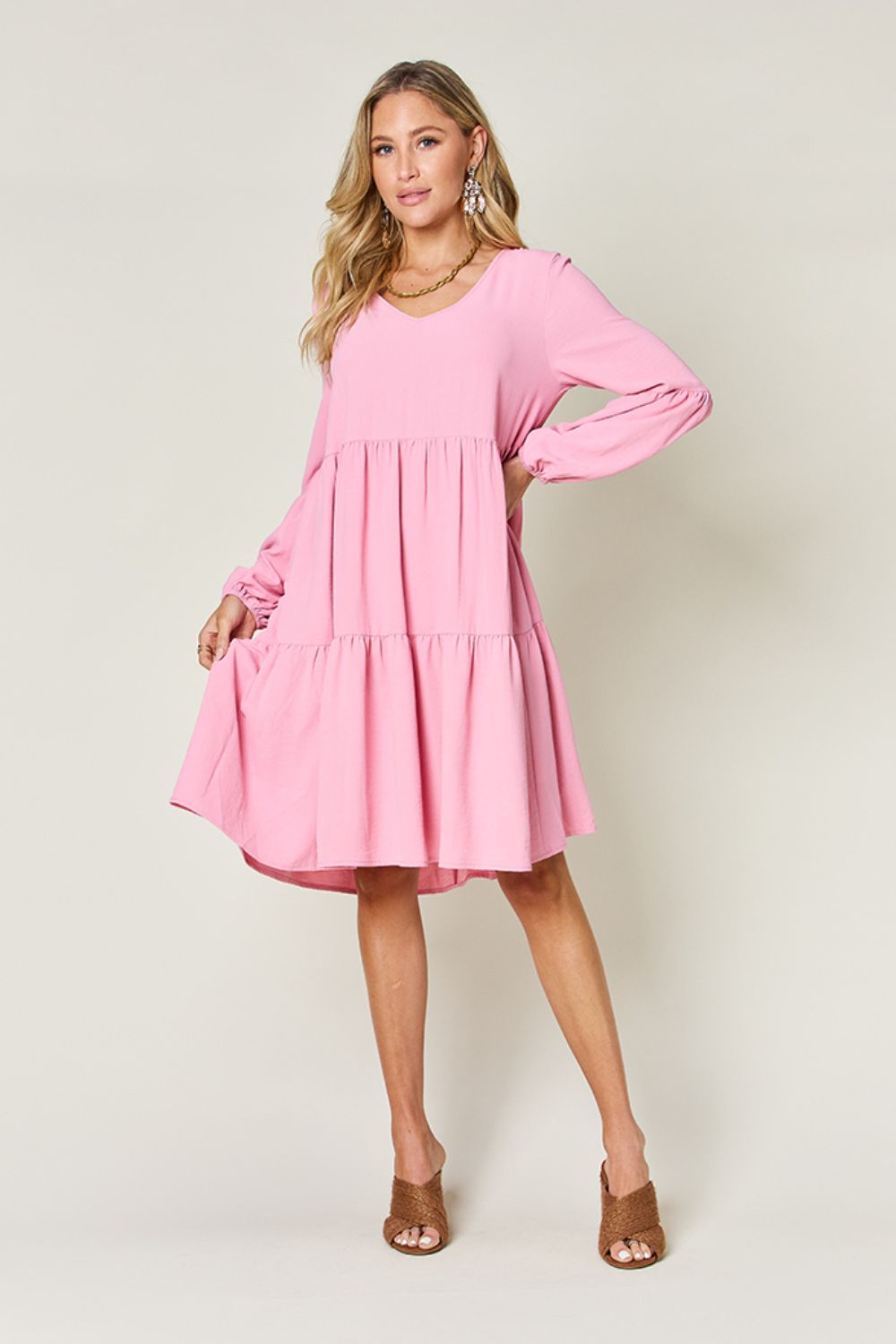 Woman wearing a pink V-neck balloon sleeve tiered dress with pockets, showcasing a stylish pocketed and ruffled design.