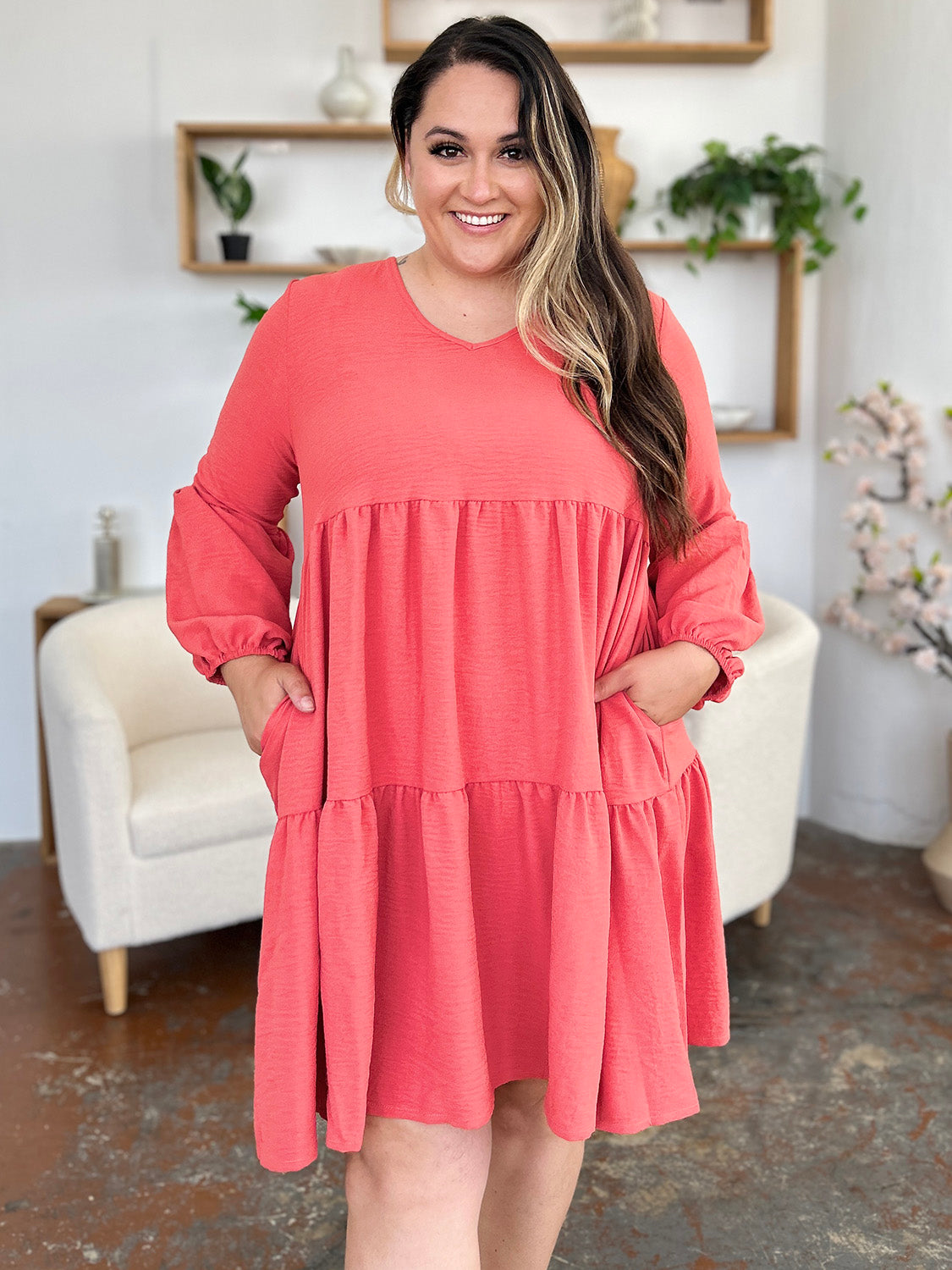 Woman wearing a coral V-neck balloon sleeve tiered dress with pockets, perfect for casual and stylish occasions.