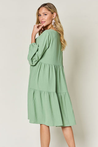 Woman wearing a green V-Neck Balloon Sleeve Tiered Dress with Pockets, showing ruffled and pocketed design on opaque fabric.