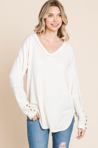 Woman wearing a white V-neck dropped shoulder blouse with buttoned cuffs, paired with blue jeans.