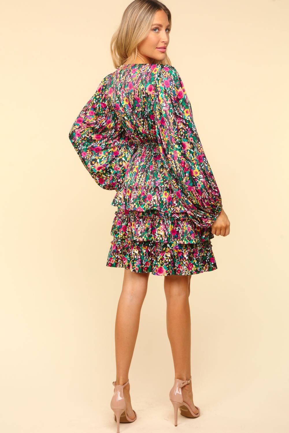 Woman wearing a V-neck satin floral layered dress with ruffled and smocked details, showcasing the colorful pattern and elegant design.