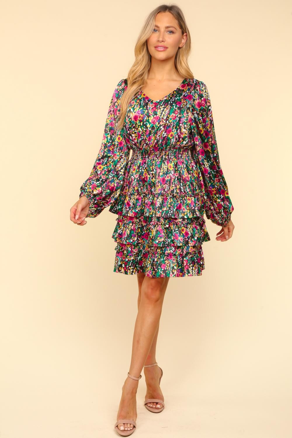 Woman wearing a V-neck satin floral layered dress with ruffled sleeves and tiered skirt, showcasing vibrant colors and elegant design.