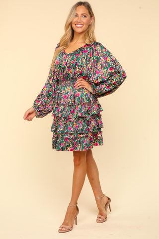 Woman wearing a V-neck satin floral layered dress with ruffled and smocked design, showcasing long sleeves and multiple tiers.