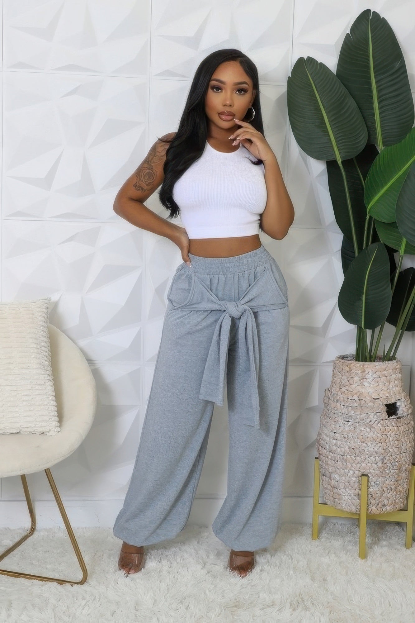 Woman wearing grey high-waisted stretch pants with a white crop top, featuring a tied waistband and wide legs, posing indoors.