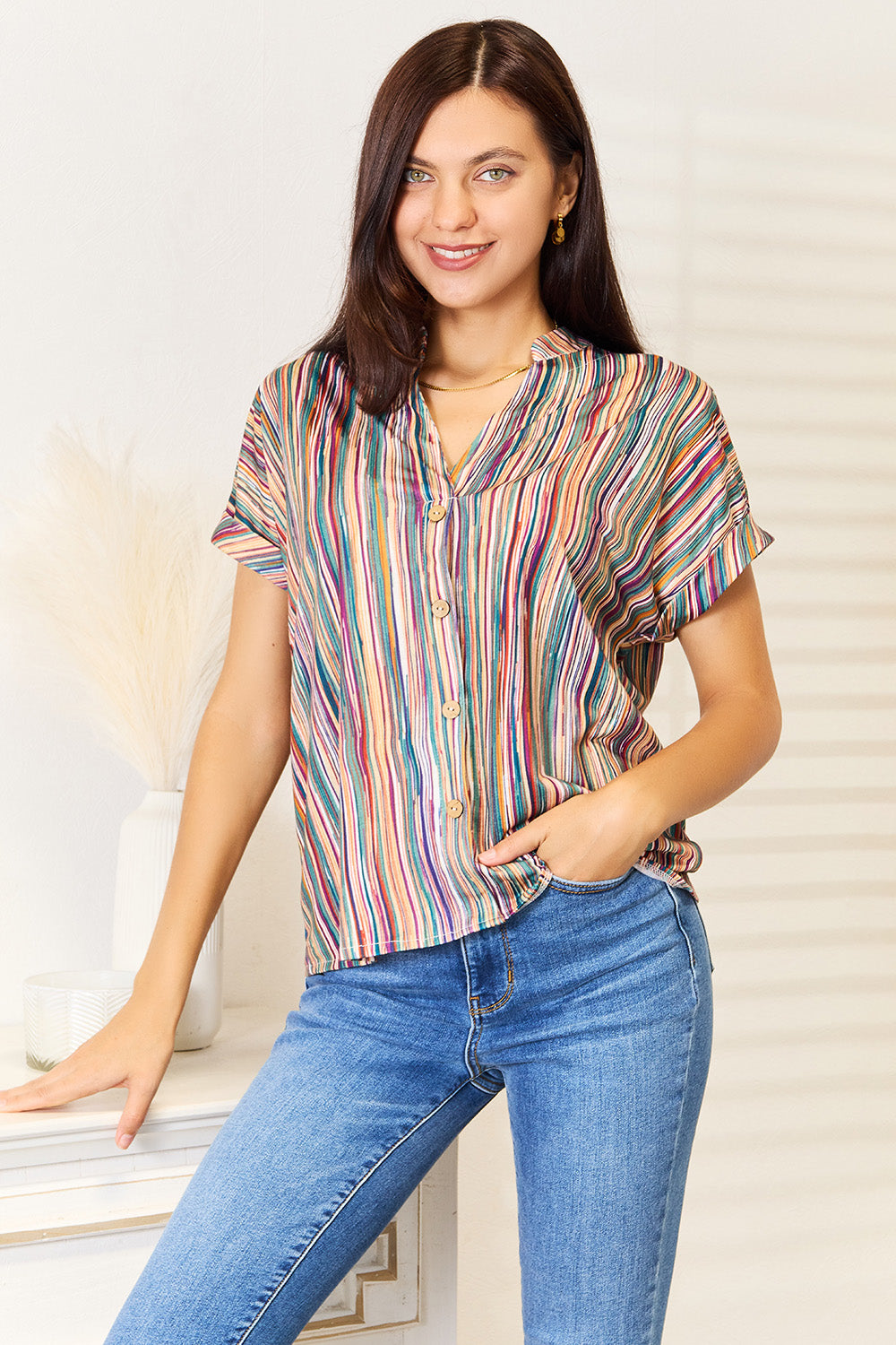 Woman wearing multicolored stripe notched neck top with jeans, showcasing vibrant design and decorative button detail.