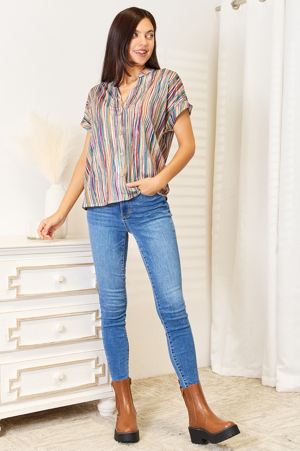 Woman wearing a multicolored stripe notched neck top with jeans and brown boots, showcasing a playful and stylish look.