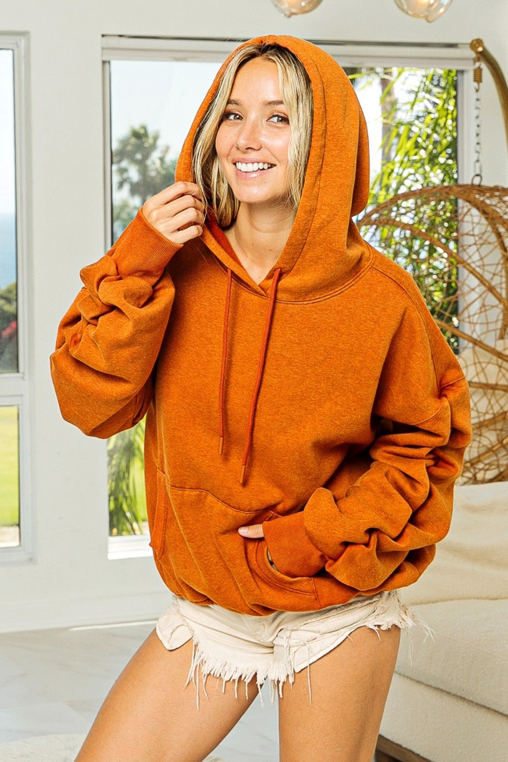 Woman wearing orange ruched long sleeve hoodie with fleece fabric, standing indoors.