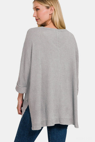 Woman wearing a gray waffle knit V-neck long sleeve slit top with high-low hem, paired with blue jeans.