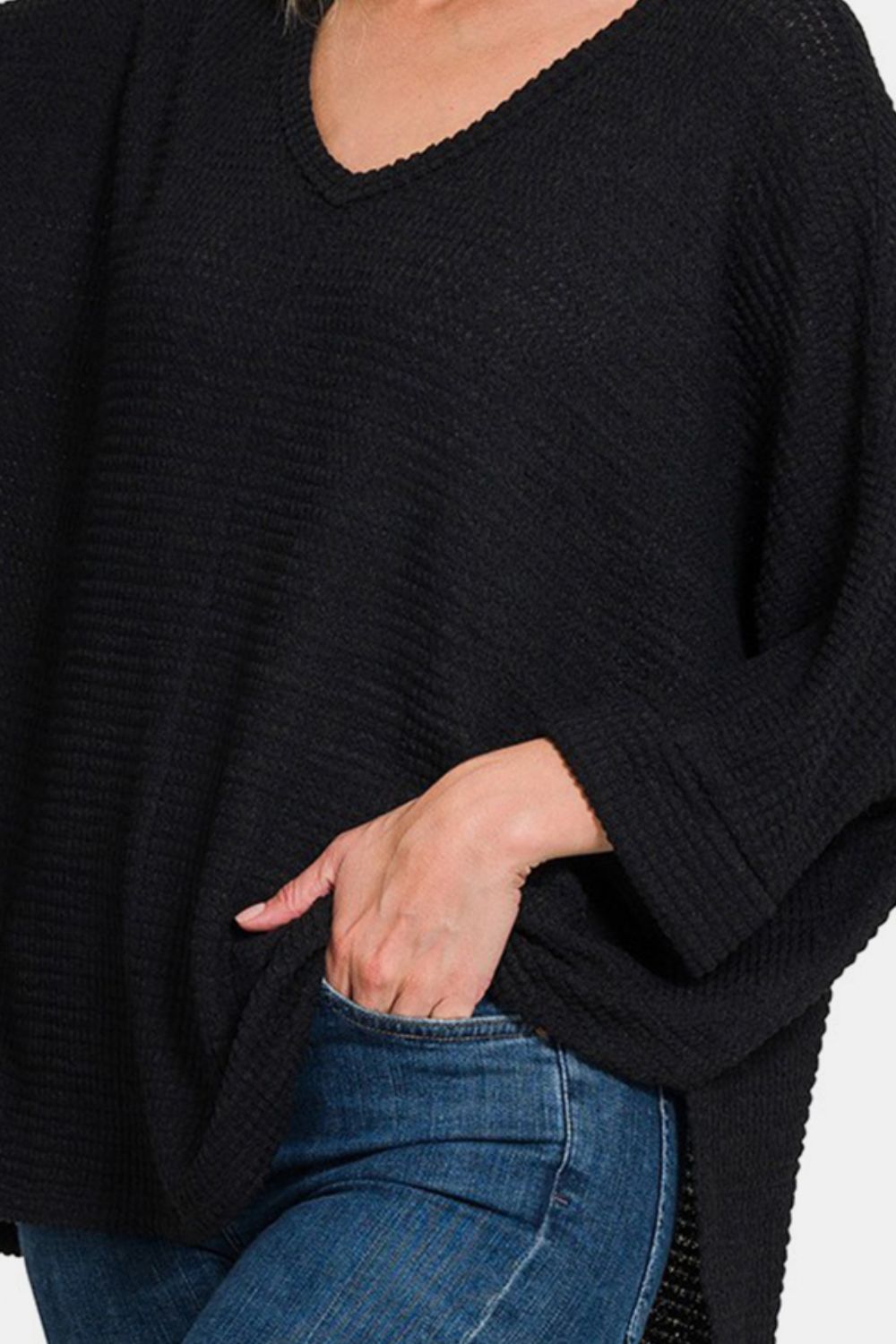 Woman in black waffle knit V-neck long sleeve slit top and jeans.