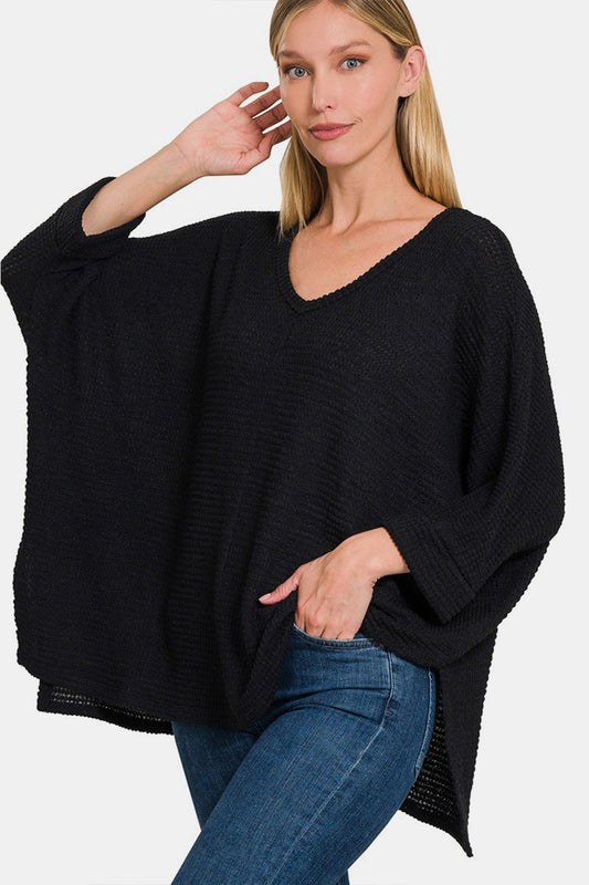 Woman wearing a black waffle knit V-neck long sleeve slit top with jeans.