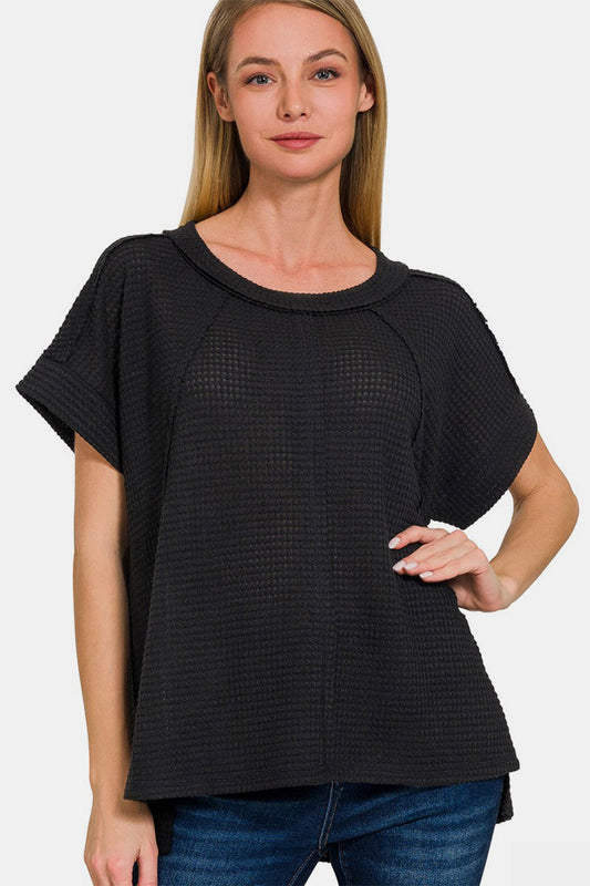 Woman wearing a black waffle-knit short sleeve t-shirt with exposed seams, paired with jeans, showcasing a casual and trendy style.