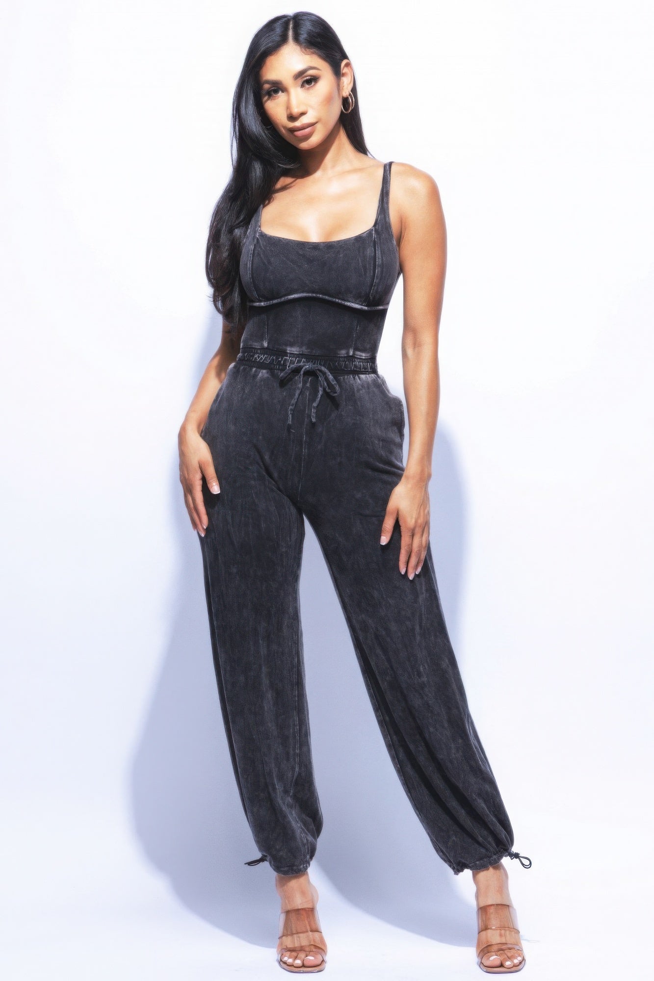 Woman in washed denim jumpsuit with adjustable ankle ties, showcasing a chic and relaxed fit against a white background.