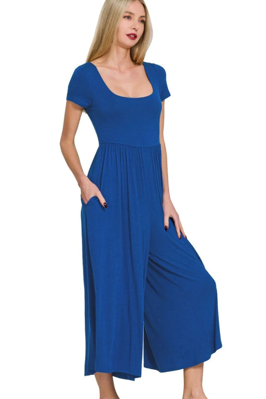 Woman in royal blue midi dress with short sleeves and scoop neckline, standing with hands in pockets against white background