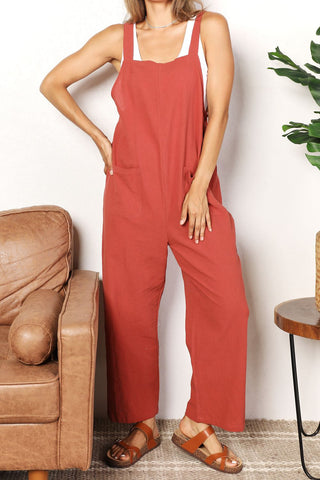 Woman wearing chic wide leg overalls with front pockets, styled with sandals, standing in a cozy living room setting.