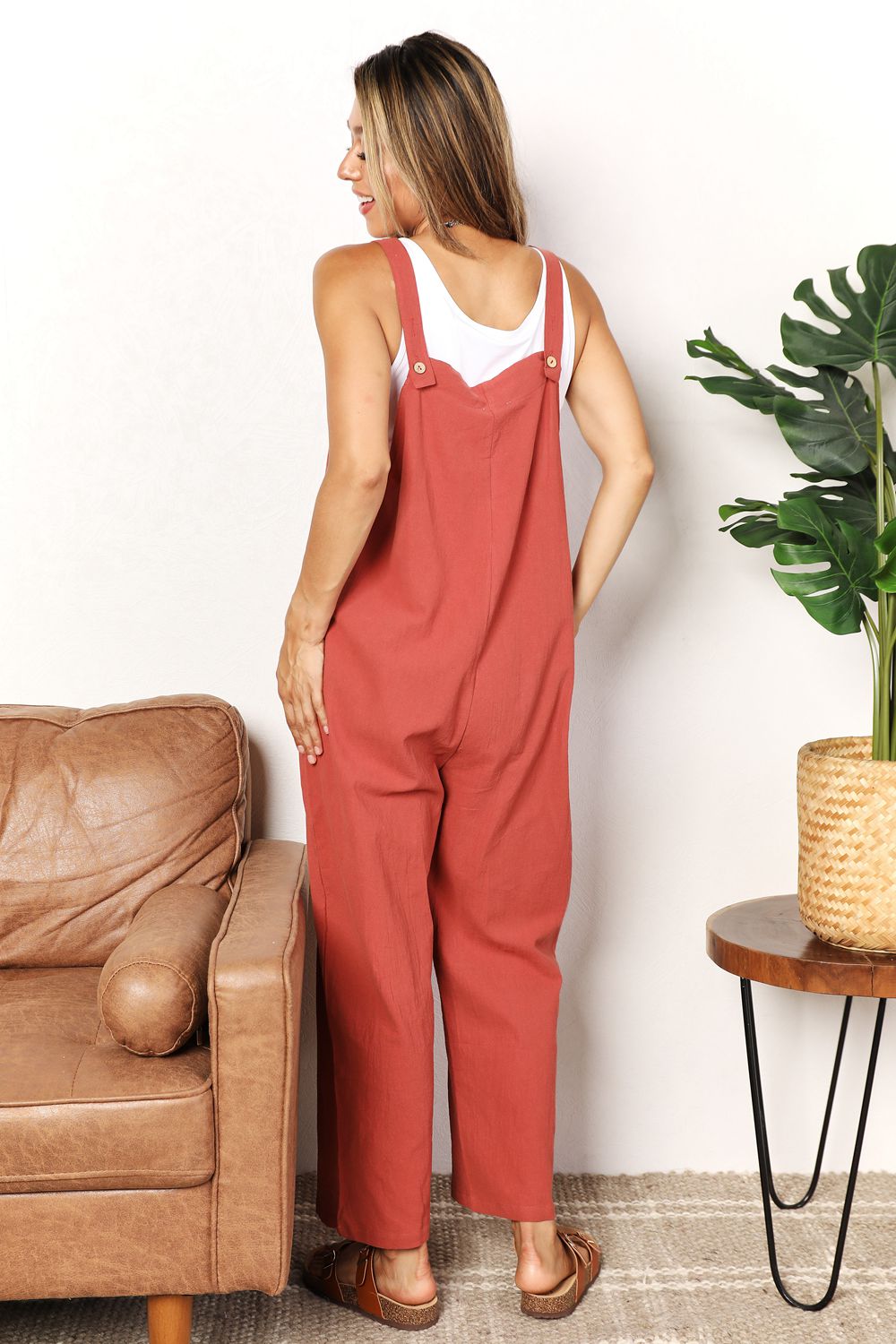 Woman wearing chic wide leg overalls with front pockets, perfect for casual wear, in a solid color, standing by a sofa and plant.