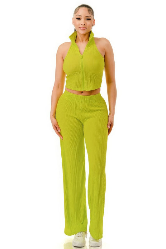 Woman wearing bright lime green ribbed two-piece set with zip-up halter top and wide-leg pants, standing against white background in white sneakers.