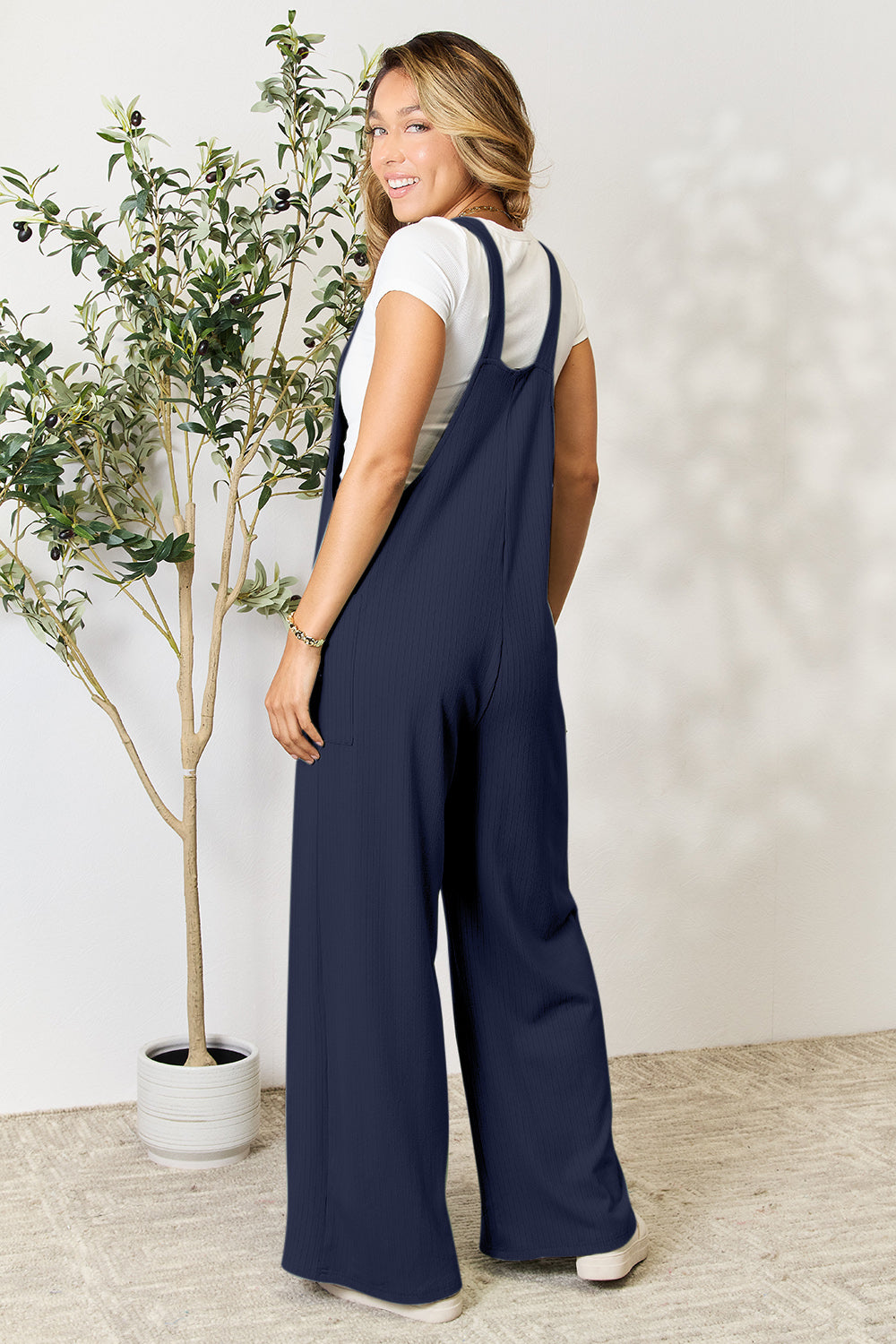 Woman wearing wide strap overalls with pockets, made of polyester, rayon, and spandex, standing near a potted plant.