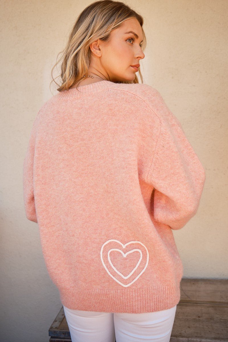 Woman wearing a pink WIFEY sweater with heart design, round neck, made of polyester, wool, and spandex.