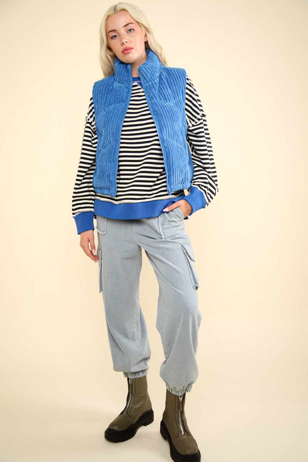 Stylish woman wearing a blue zip-up padded corduroy puffer vest jacket over a striped top and cargo pants.