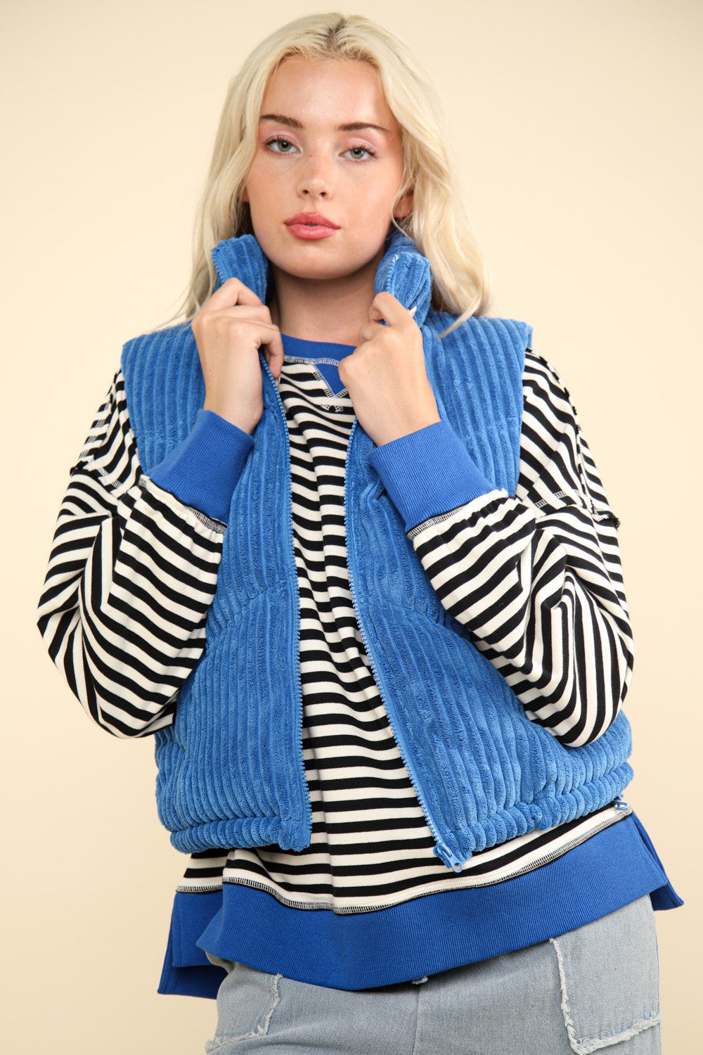 Woman wearing a trendy blue zip-up padded corduroy puffer vest jacket over a striped shirt, showcasing stylish winter layering.