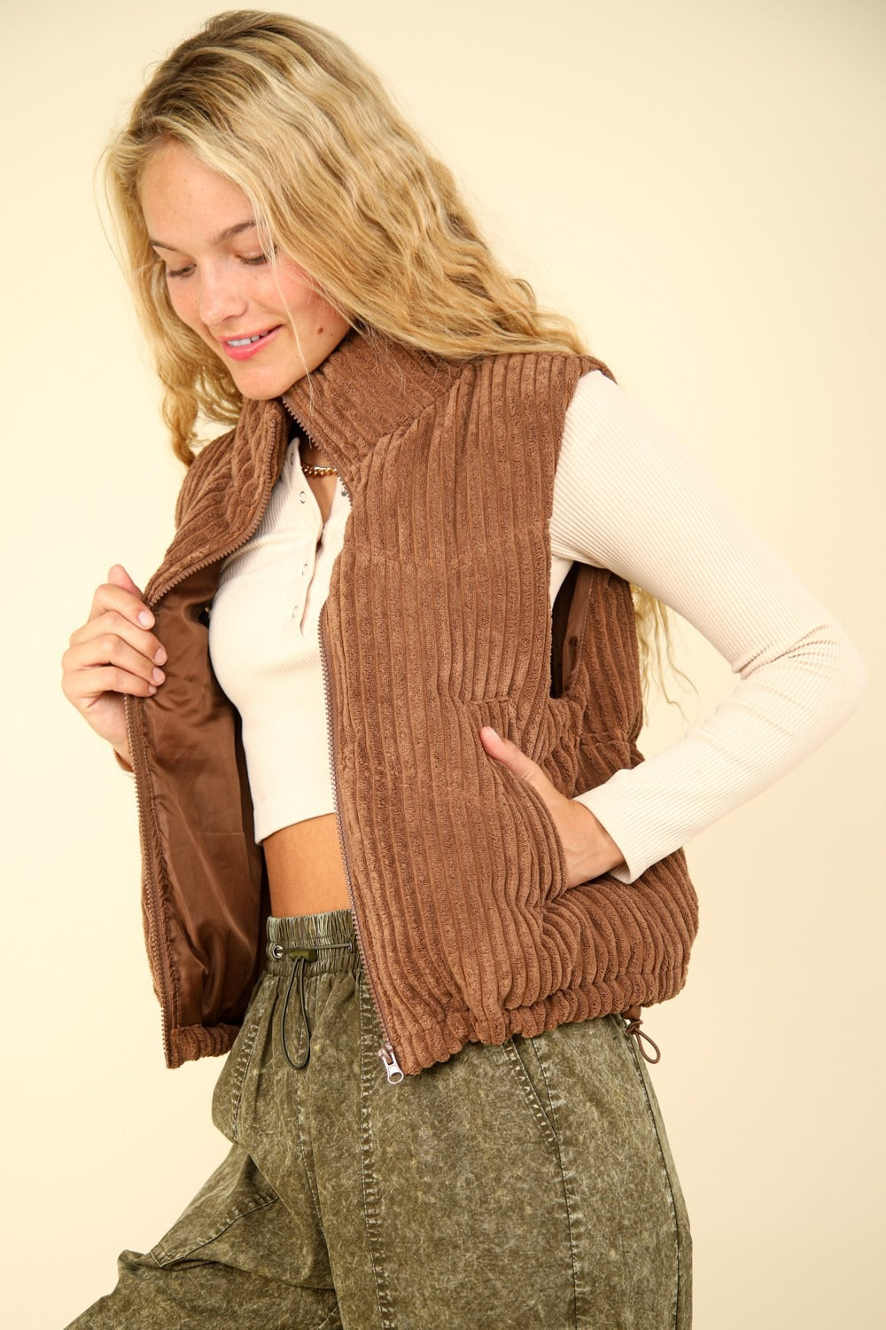 Woman wearing a brown zip-up padded corduroy puffer vest with zig-zag pattern and high neck design.