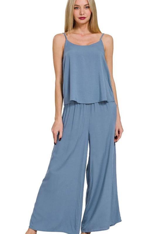 Woman in dusty blue two-piece set with spaghetti strap camisole top and wide-leg palazzo pants, standing against white background