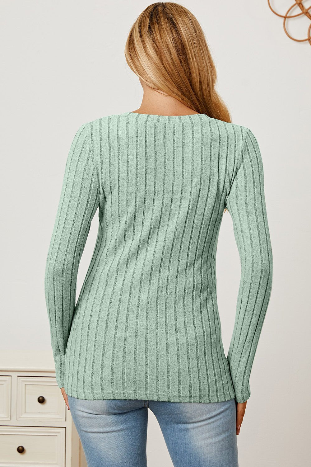 Woman in mint green ribbed V-neck long sleeve T-shirt and jeans, facing away, showcasing back style and fit.