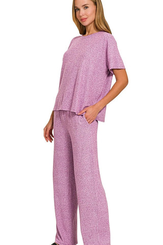 Woman wearing a pink heathered two-piece loungewear set with short-sleeve top and wide-leg pants, standing against white background with hand in...